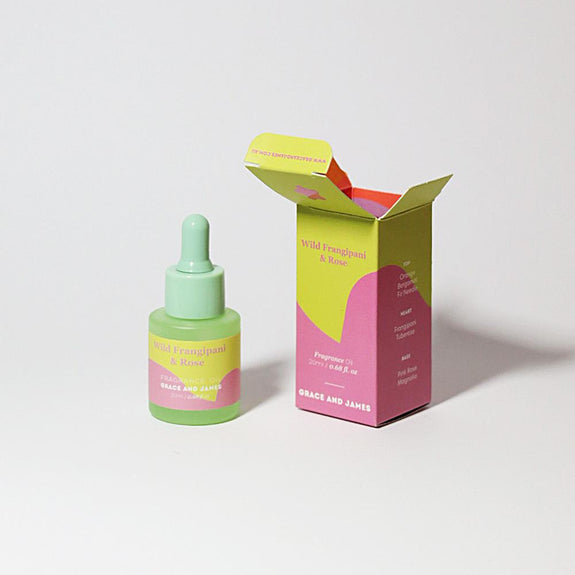 Green dropper bottle with pink label next to its open pink and yellow box on a light gray background