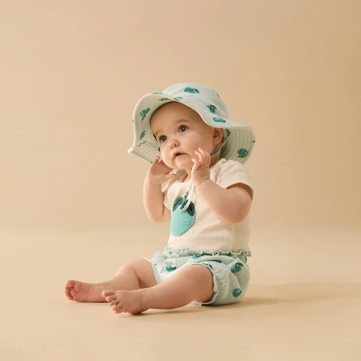 Baby wearing a matching outfit with a green and white pattern on a beige background