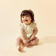 Baby in a lace romper sitting on a beige background