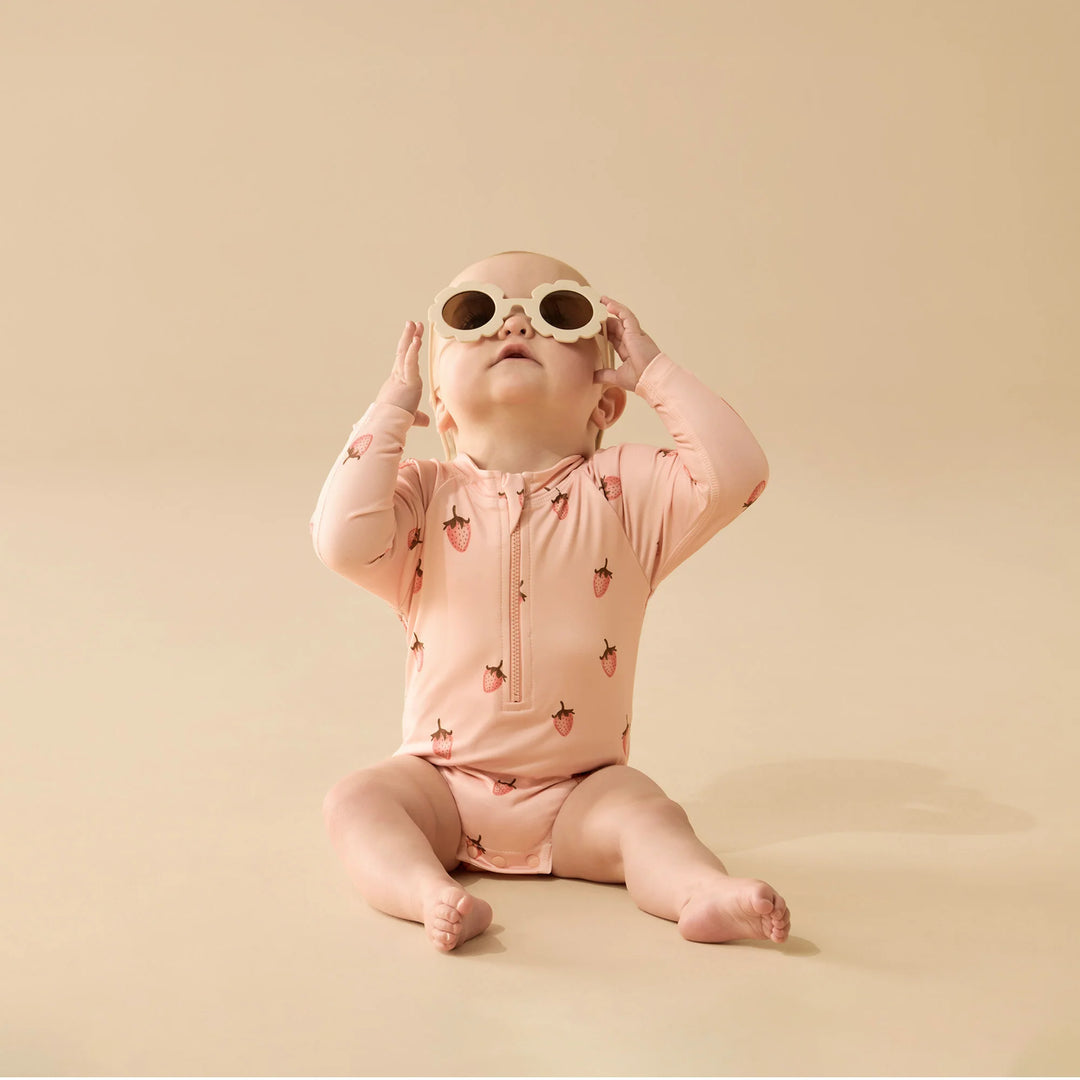 Baby wearing a pink Wilson & French strawberry-patterned onesie and sunglasses on a beige background