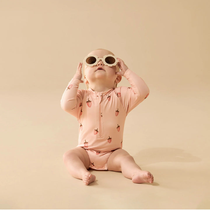 Baby wearing a pink Wilson & French strawberry-patterned onesie and sunglasses on a beige background