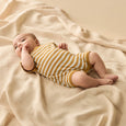 Baby in a yellow and white Wilson & frenchy striped outfit lying on a beige blanket