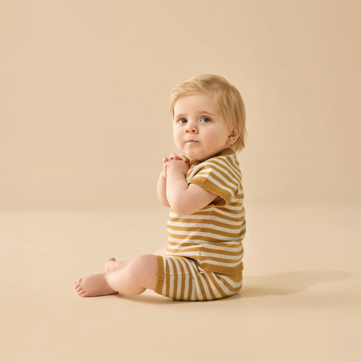 Baby wearing a wilson & frenchy yellow and white striped outfit on a beige background