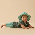 Baby wearing a green and white striped hat and outfit on a beige background