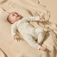 Baby lying on a beige blanket wearing a Wilson & frenchy white onesie with small patterns.