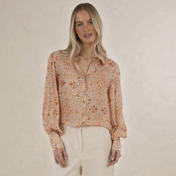 Woman wearing a floral blouse and beige pants on a plain background