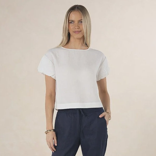 Woman wearing a white top and navy pants on a beige background