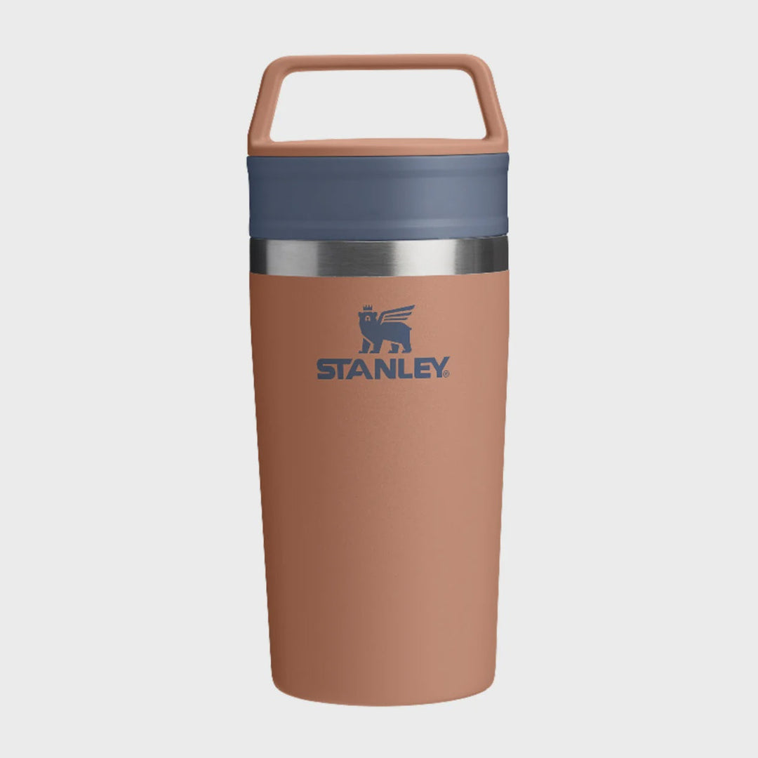 Stanley insulated travel tumbler in a dusty terracotta color with a slate blue lid and handle, featuring a silver metallic band and the Stanley logo on the front.