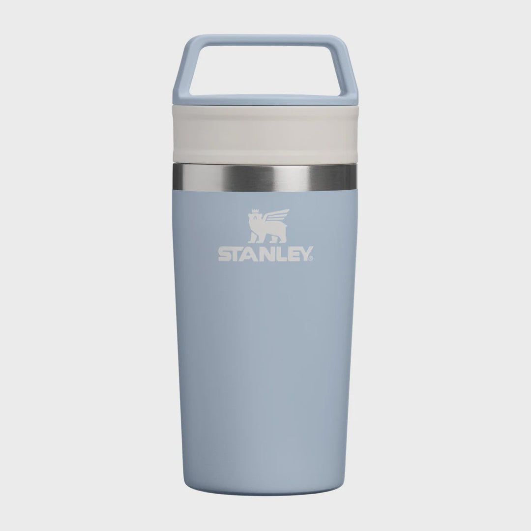 A light blue Stanley travel tumbler with a matching lid and carry handle, featuring a silver stainless steel band and the white Stanley logo on the front, set against a solid light gray background.