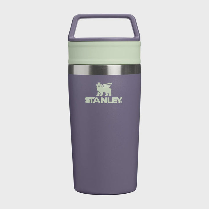 Stanley vacuum-insulated travel tumbler in a muted purple color, featuring a light sage green lid band and a matching carrying loop on a light gray background.