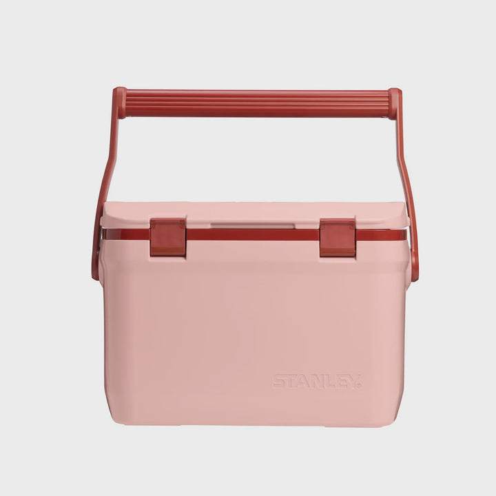 A light pink Stanley cooler with a terracotta red handle and latches, shown against a light gray background.