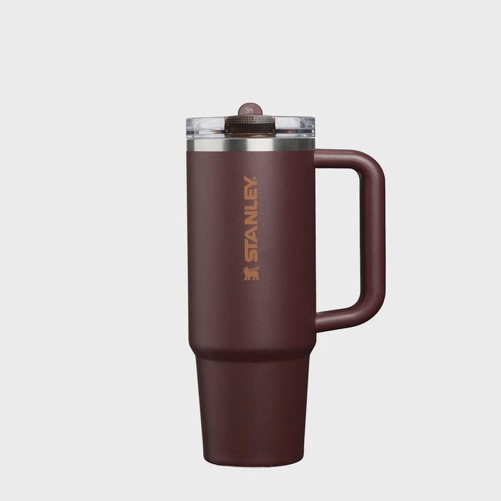 Stanley travel mug in a dark brown color with a matching handle and lid, featuring the Stanley logo printed vertically on the side, set against a light gray background.