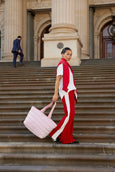 Woman in red and white outfit holding a pink bag on steps of a classical building