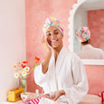 Woman in a bathrobe with a colorful towel on her head in a bathroom setting.