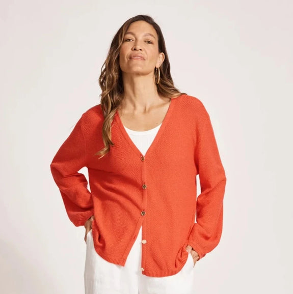 Woman wearing a red eb & ive cardigan over a white top and pants on a white background