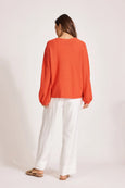 Woman wearing an orange top and white pants on a plain background