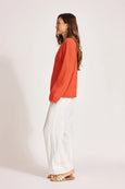 Woman wearing an orange sweater and white pants on a plain background