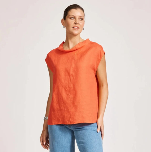 Woman wearing an eb & ive orange sleeveless top and blue jeans on a light background