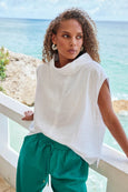 Woman wearing a eb & ive white top and green pants by a coastal railing