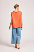 Person wearing an eb & ive orange sleeveless top and blue pants on a light background