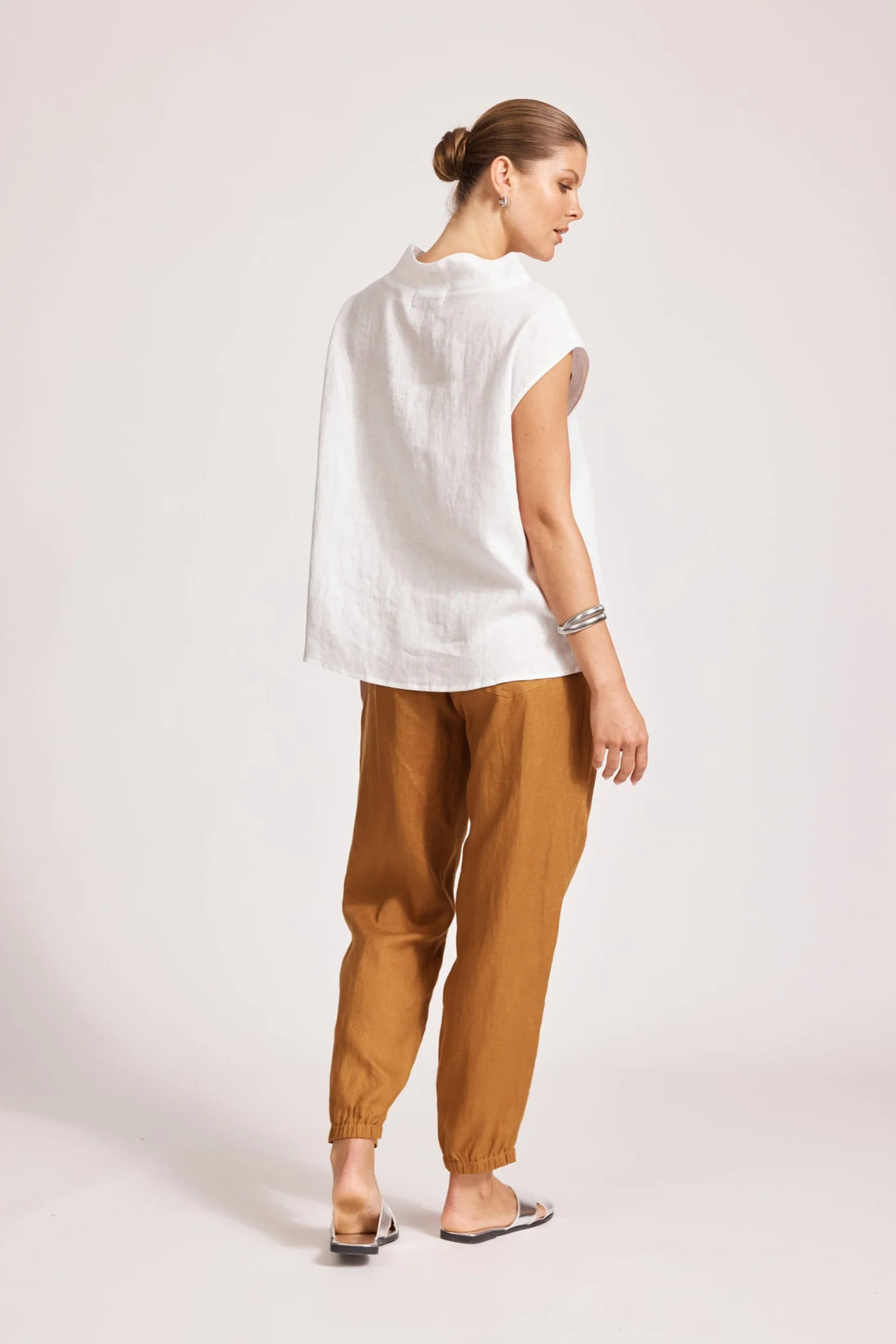 Woman wearing a eb & ive white top and brown pants on a light pink background