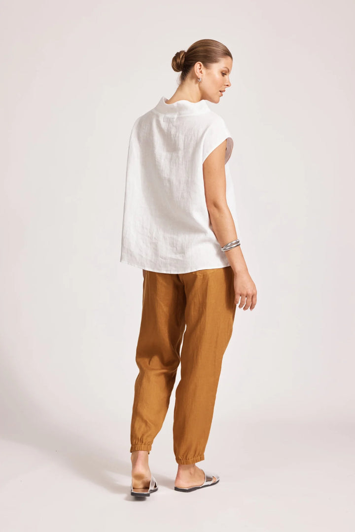 Woman wearing a eb & ive white top and brown pants on a light pink background