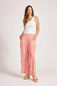 Woman wearing a white sleeveless top and eb & ive red and white striped pants on a plain background