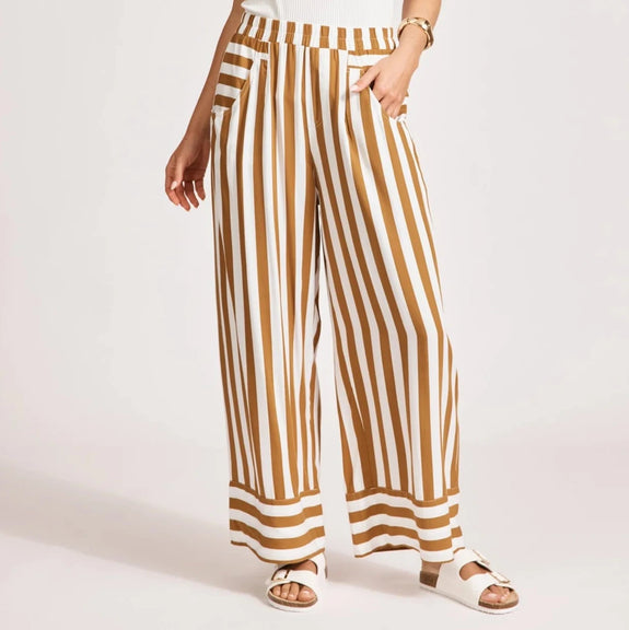 Woman wearing a white sleeveless top and eb & ive brown and white striped pants on a light pink background