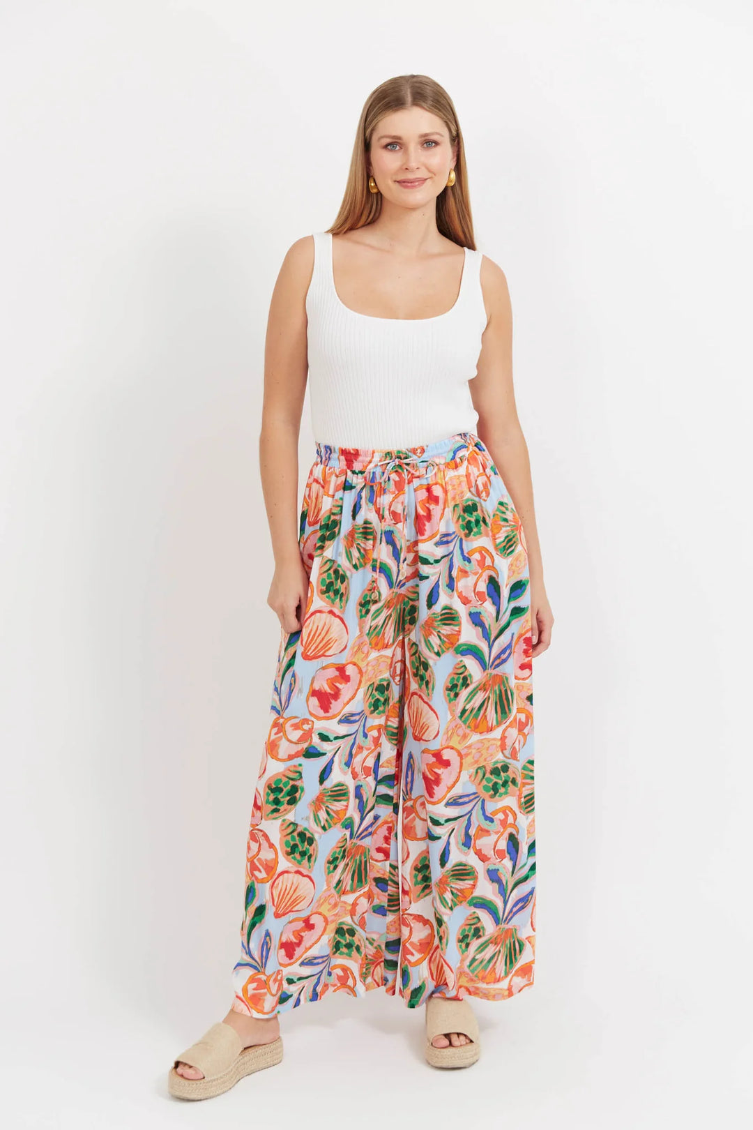 Woman wearing a white tank top and colorful floral Haven pants on a white background
