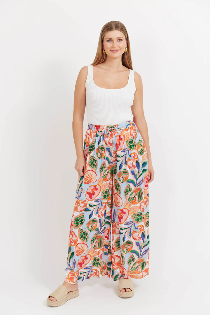Woman wearing a white tank top and colorful floral Haven pants on a white background