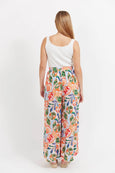 Woman wearing a white sleeveless top and colorful floral Haven pants on a white background