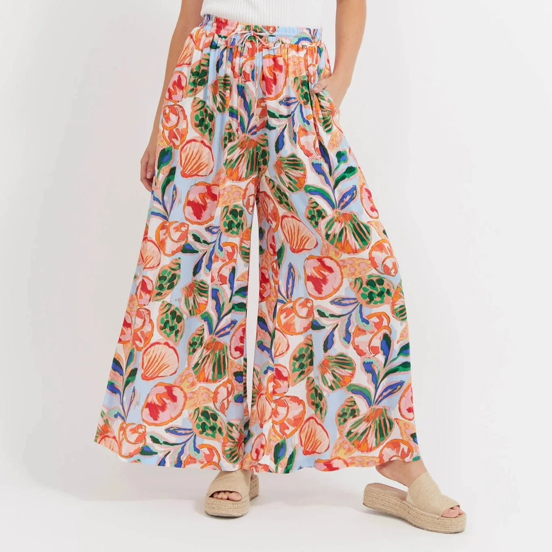 Woman wearing a white top and colorful floral Haven pants on a white background