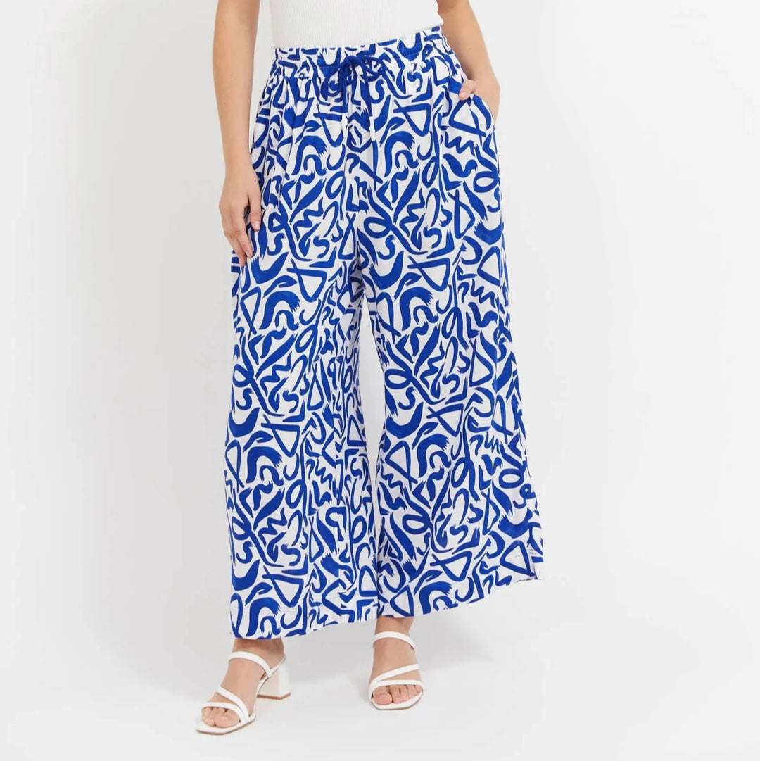 Woman wearing a white sleeveless top and Haven blue patterned pants on a white background