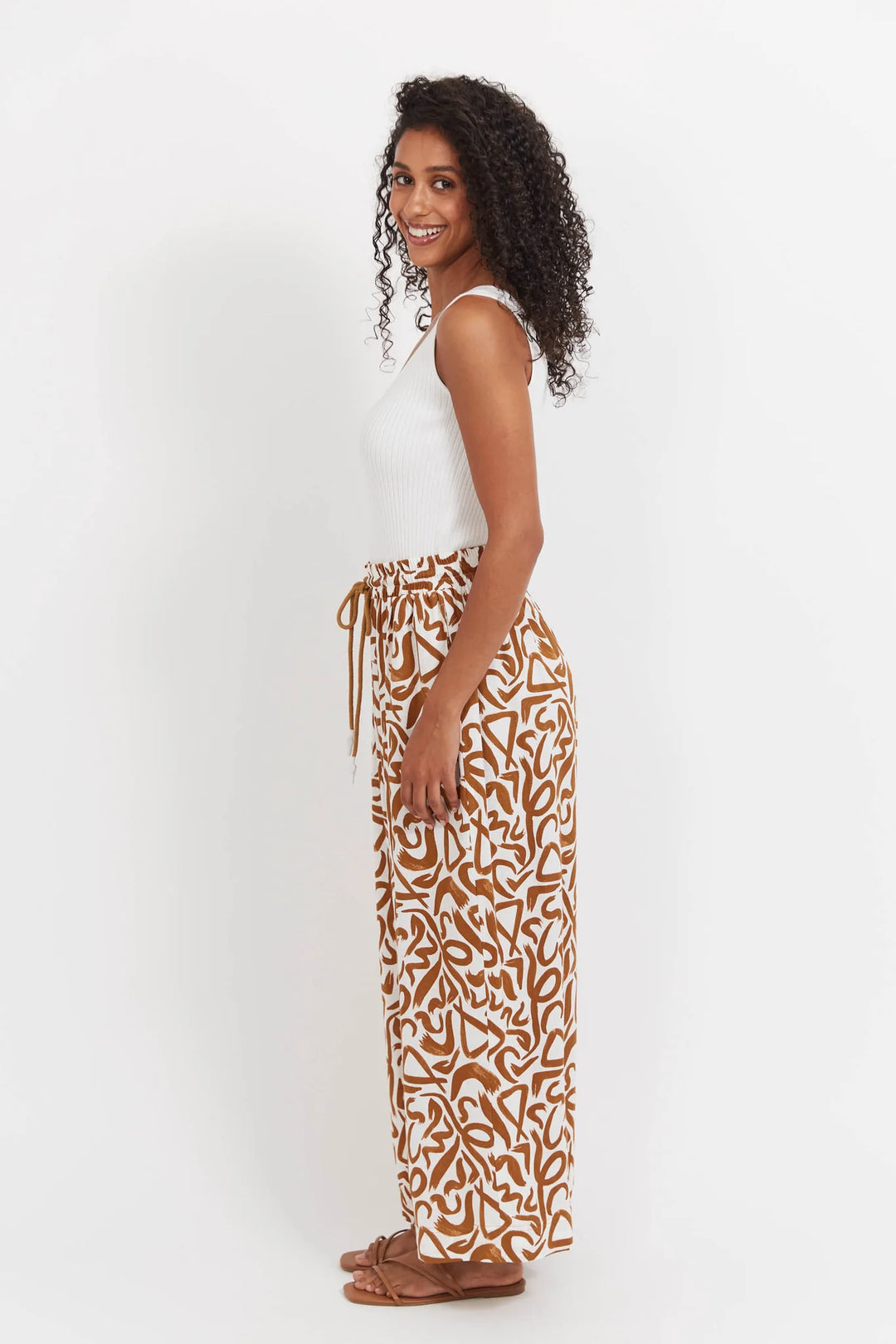 Woman wearing a white sleeveless top and haven patterned pants on a white background