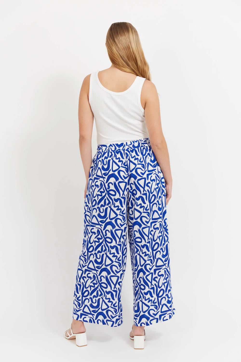 Woman wearing Haven blue patterned pants and a white top on a white background