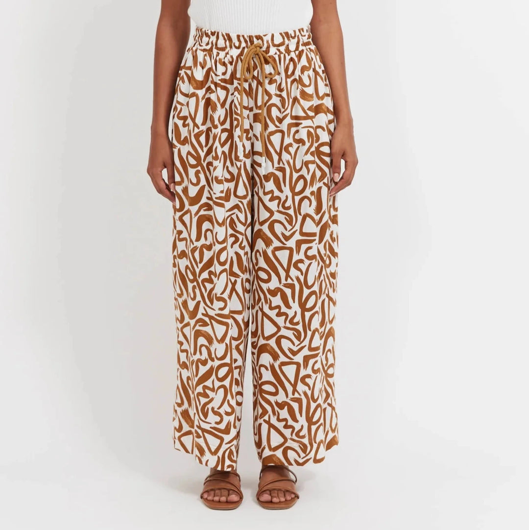 Woman wearing a white tank top and Haven patterned pants on a white background