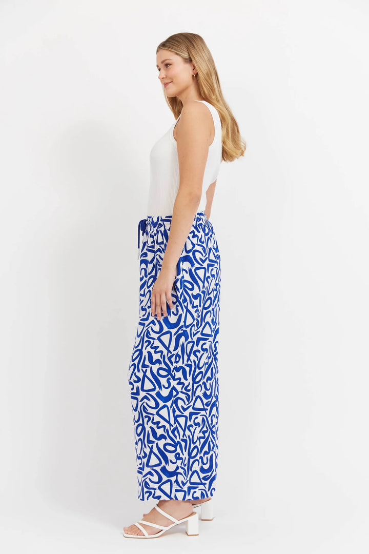 Woman wearing a white sleeveless top and Haven blue patterned pants on a white background