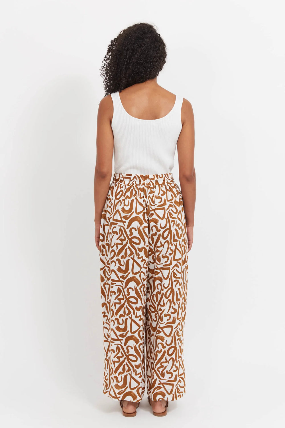 Woman wearing a white top and haven patterned pants on a white background