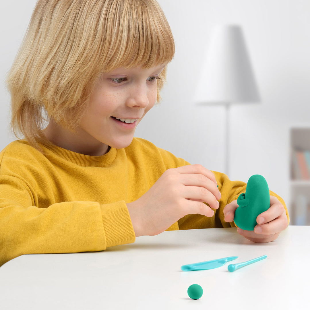 Child playing with green play dough and tools on a white surface.