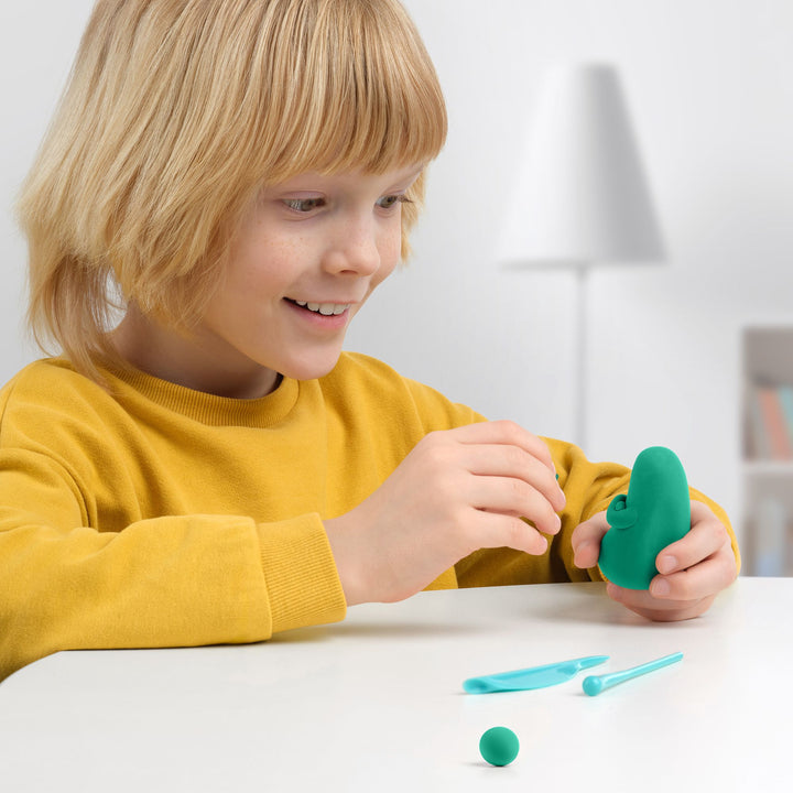 Child playing with green play dough and tools on a white surface.