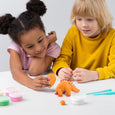 Two children playing with orange play-doh and a dinosaur toy on a white surface.