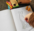 Child coloring a picture of a cat in a coloring book with crayons.