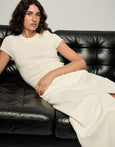 Woman in a white dress sitting on a black leather couch against a plain background