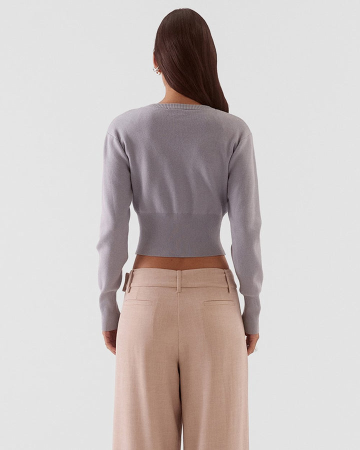 A woman shown from the back wearing a light gray long-sleeve cropped knit top and beige wide-leg trousers, against a plain light gray studio background.
