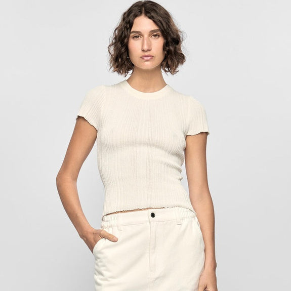 Woman wearing a white top and cream-colored pants against a light gray background