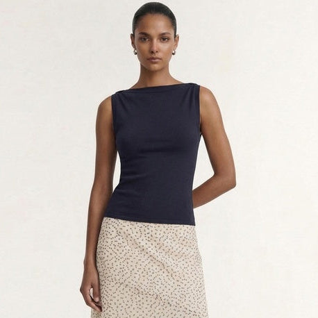 A model stands against a plain light background wearing a sleeveless dark navy top and a cream wrap-style midi skirt with a small beige floral print and an asymmetrical hem.