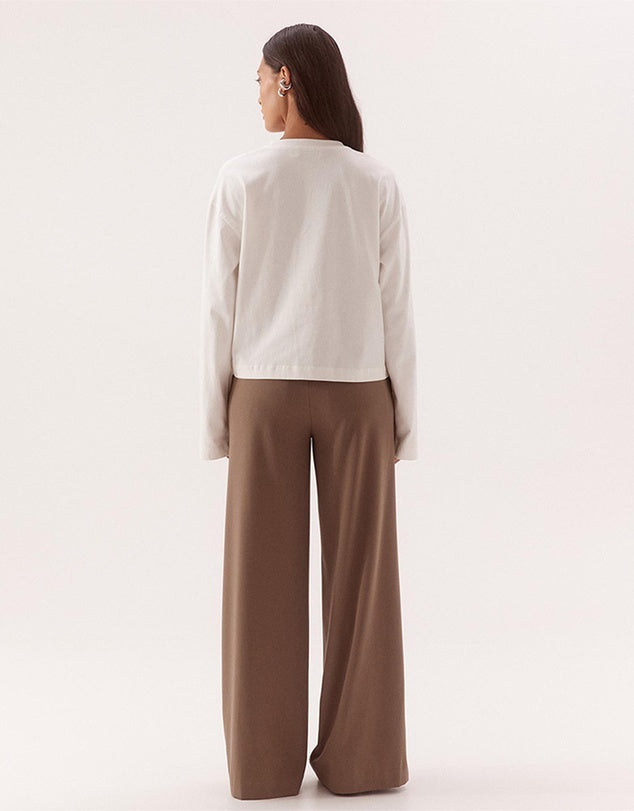 A woman shown from the back wearing a white cropped long-sleeve top and brown wide-leg pants against a plain light background.