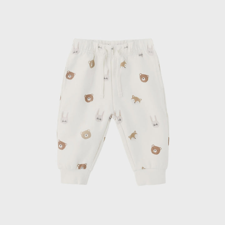 A pair of baby jogger pants in off-white, featuring an all-over print of cute brown teddy bears, foxes, and rabbits. The pants have an elastic waistband with a white drawstring and ribbed ankle cuffs, shown against a light gray background.