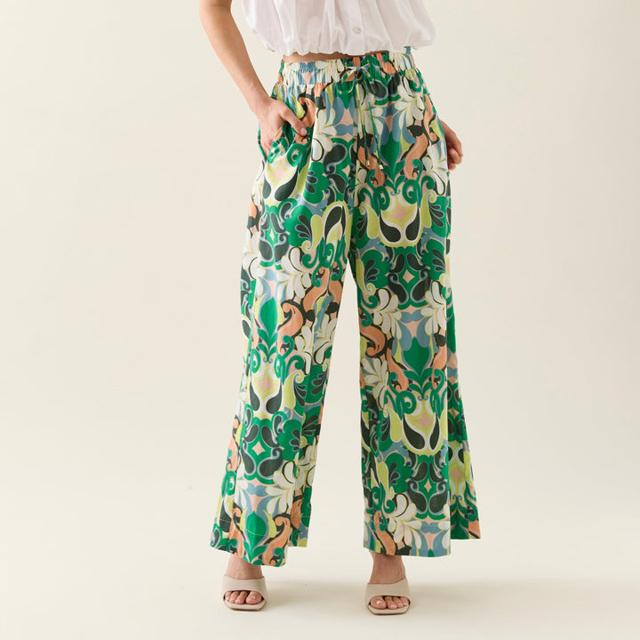 Woman wearing a white isle of mine top and colorful patterned pants on a plain background 