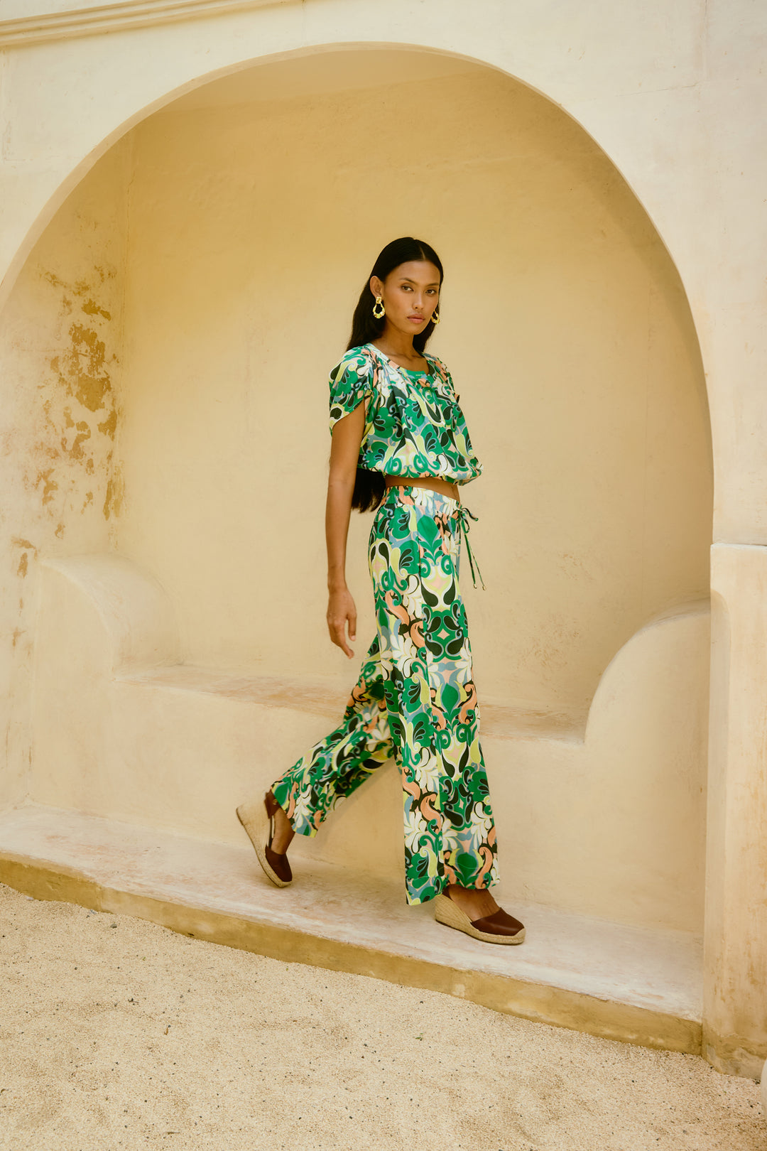 Woman in isle of mine green floral outfit standing in an arched stone doorway.